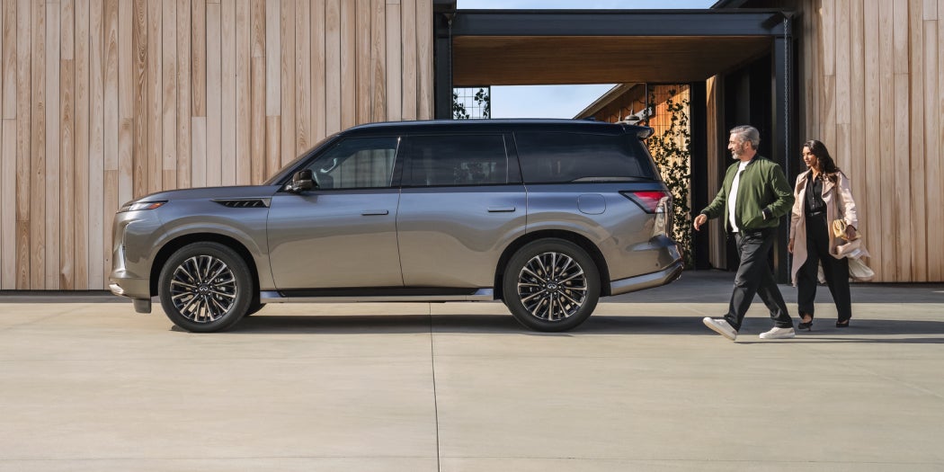 Two people walking next to a parked silver SUV in front of a modern wooden building.